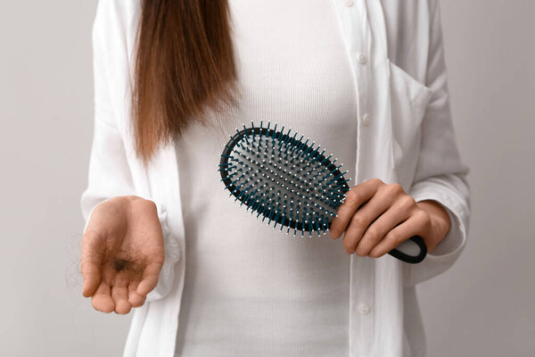 Женщина держит расческу и сгусток волос на сером фоне. Концепция выпадения волос