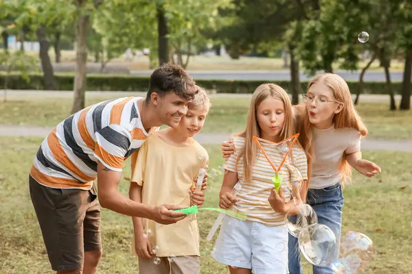 Parkta sabun köpüğü üfleyen sevimli çocuklu mutlu bir aile.