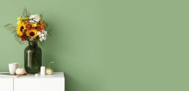 İçinde sonbahar çiçekleri, yanan mumlar ve yeşil duvarın yanında balkabakları olan beyaz büfe. Tasarım için pankart