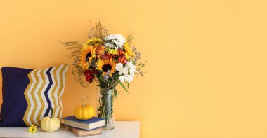 İçinde bir buket sonbahar çiçeği olan çekmeceler, sarı duvarın yanında kitaplar ve balkabakları. Tasarım için pankart