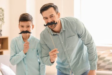 Evde kağıt bıyıklı babasının ve küçük oğlunun portresi.