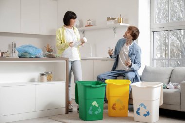 Mutfaktaki çöpleri düzenleyen çöp konteynırları olan genç bir çift. Geri dönüşüm kavramı