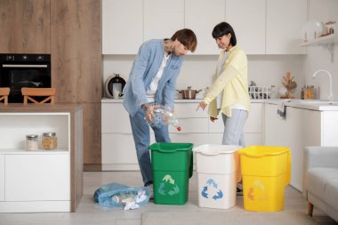 Mutfaktaki çöpleri düzenleyen çöp konteynırları olan genç bir çift. Geri dönüşüm kavramı