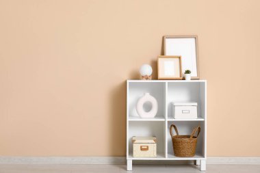 Bej duvarın yanında resim çerçeveli ve raf üniteli şık bir oda.