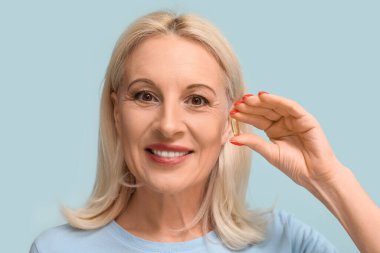 Açık mavi arka planda balık yağı haplı olgun bir kadın.