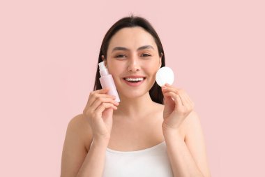 Pamuklu pedi olan mutlu genç bir kadın ve pembe arka plandaki makyajı silmek için mikiler suyu.