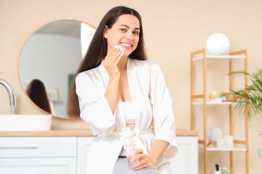 Beautiful young happy woman with cotton pad and bottle of micellar water at home