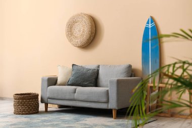 Gri kanepe ve sörf tahtası şık oturma odasındaki bej duvarın yanında.