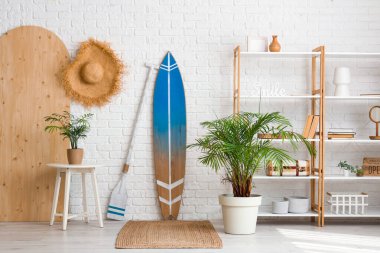 Beyaz tuğla duvarın yanında sörf tahtası ve raf ünitesi olan modern tarz bir oda.