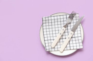 Tabak, çatal bıçak takımı ve mor arkaplandaki kareli peçeteyle masa ayarları