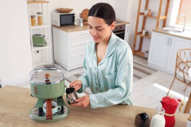 Mutfakta modern makineyle taze kahve yapan genç ve güzel bir kadın.