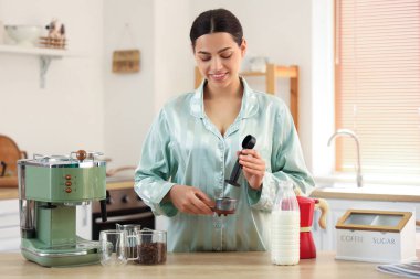 Mutfakta modern makineyle taze kahve yapan genç ve güzel bir kadın.