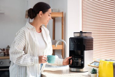 Mutfakta fincanı ve modern kahve makinesi olan genç ve güzel bir kadın.