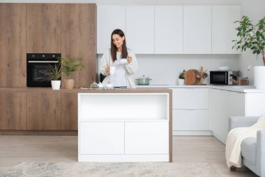 Modern mutfağın yanında fincana çay dolduran genç bir kadın.