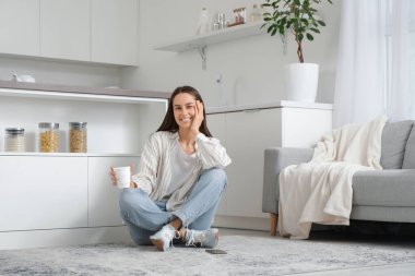 Genç ve güzel, modern mutfakta yerde oturuyor.