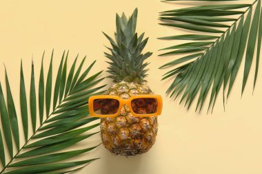 Güneş gözlüklü taze ananas ve sarı arka planda palmiye yaprakları.