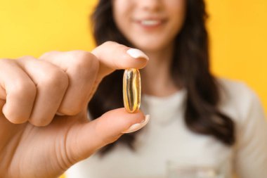 Sarı arka planda balık yağı kapsülü olan genç ve güzel bir kadın. Yakın plan.