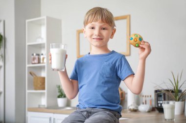 Bir bardak süt ve kurabiyeyle mutfak tezgahında oturan küçük çocuk.