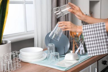Mutfakta bulaşık takımının yanında temiz bardakları tutan kadın eller.