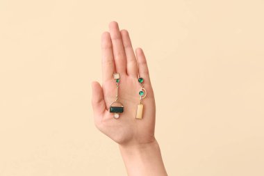 Bej arka planda güzel küpeleri olan bir kadın eli.