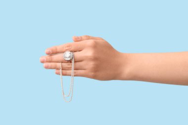 Mavi arka planda güzel yüzüklü ve kolyeli bir kadın.