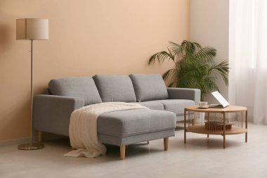 Konforlu kanepe, çiçek ve oturma odasındaki bej duvarın yanındaki kahve masası.