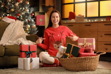 Evde yerde oturan hediye kutularıyla mutlu genç bir kadın. Noel konsepti
