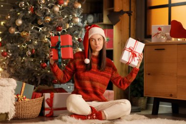 Noel Baba şapkalı genç mutlu kadın evde hediye kutularıyla yerde oturuyor. Noel konsepti