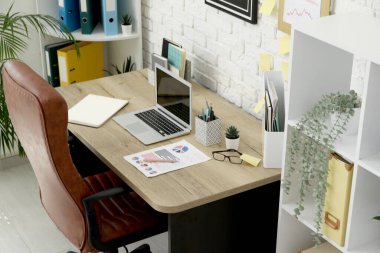 Ofis içi işyeri, kahverengi koltuk, modern dizüstü bilgisayar ve raf ünitesi, yakın çekim.