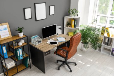 Çalışma yeri, koltuk, modern bilgisayar, ev bitkisi ve raflama ünitesi siyah duvarın yanında.