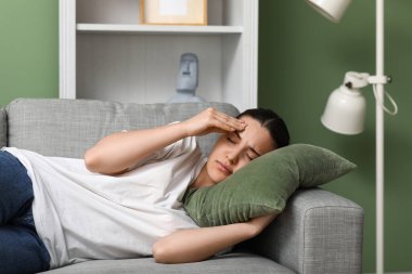 Genç kadın baş ağrısı çekiyor ve evdeki kanepede yatıyor.