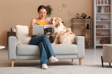 Genç bayan, oturma odasındaki yumuşak kanepede sevimli bir çoban köpeğiyle dergi okuyor.