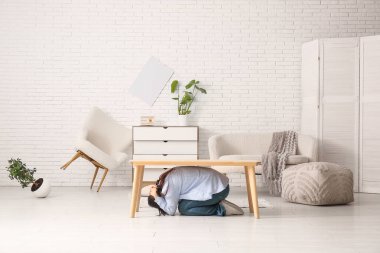 Depremden sonra hasarlı oturma odasında masanın altında saklanan genç bir kadın.