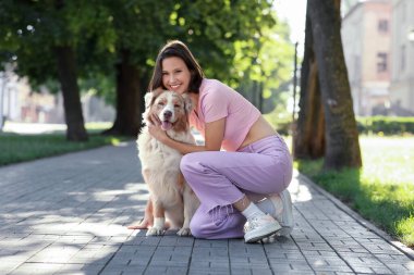 Güzel Avustralya çoban köpeğiyle parkta oturan mutlu genç kadın.