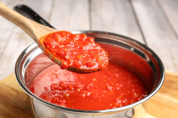 Saucepan and spoon with tasty tomato sauce on table, closeup
