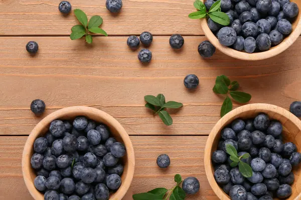 Tatlı taze yaban mersinli kaseler ve ahşap arka planda yapraklar