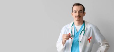 Young male doctor with red ribbons on grey background. AIDS awareness concept clipart