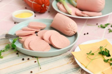 Tabakta haşlanmış sosis, pembe fayans üzerinde yeşil soğan ve sos.