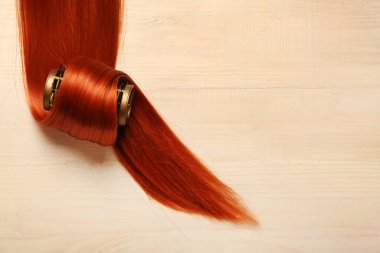 Hafif ahşap arka planda bukleli kızıl saç teli, yakın plan.