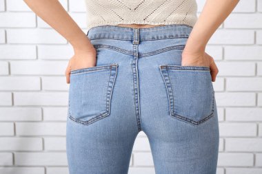 Hafif tuğlalı duvarın yanında şık kotlu genç bir kadın.