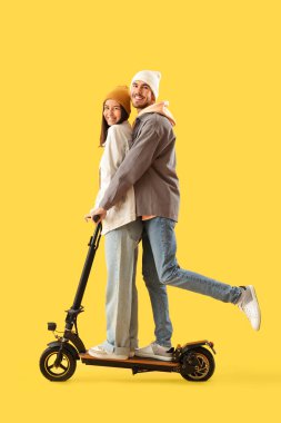 Sarı arka planda elektrikli scooter kullanan genç çift.