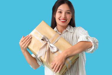 Mavi arka planda hediye kutusu olan güzel bir Asyalı kadın.