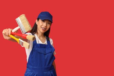 Kırmızı arka planda fırçaları olan Asyalı mutlu kadın ressam.