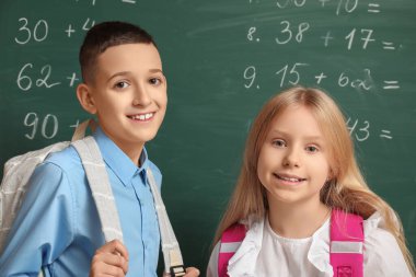 Sınıfta tahtaya yakın sırt çantalı sevimli öğrenciler.