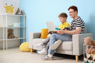 Babasıyla küçük bir çocuk evdeki kanepede dizüstü bilgisayar kullanıyor.