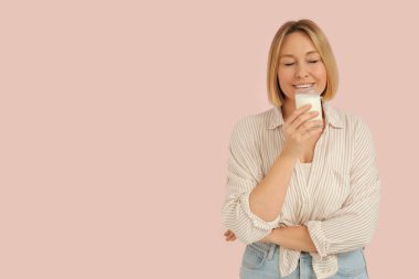 Pembe arka planda bir bardak taze sütle güzel bir genç kadın.