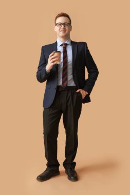 Gözlüklü genç adam kahverengi arka planda bir fincan kahve tutuyor.