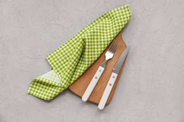 Gri grunge arkaplan üzerinde kareli peçete, çatal bıçak ve ahşap tahta ile masa ayarı