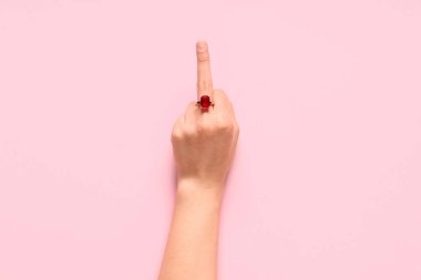 Pembe arka planda orta parmağını gösteren güzel yüzüklü bir kadın eli.