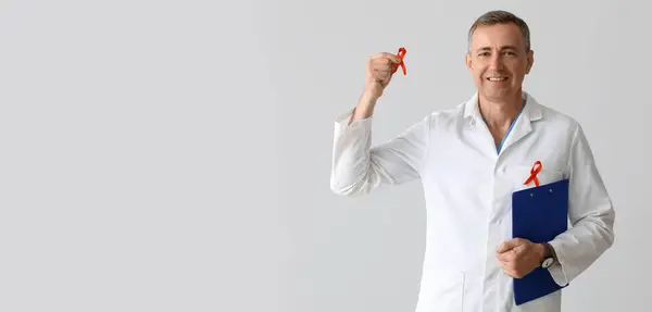 stock image Mature male doctor with red ribbons and clipboard on grey background. AIDS awareness concept